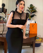 Woman in elegant black dress with sheer polka-dot top, standing indoors near shopping bags, ZAPDRESS fashion