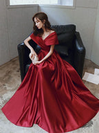 Woman in elegant red off-shoulder satin gown sitting on black chair, ZAPDRESS fashion
