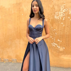 Woman in navy satin evening dress with slit posing by rustic orange wall, ZAPDRESS fashion