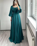Woman wearing a teal maxi dress with long sleeves in a modern, bright room, ZAPDRESS fashion