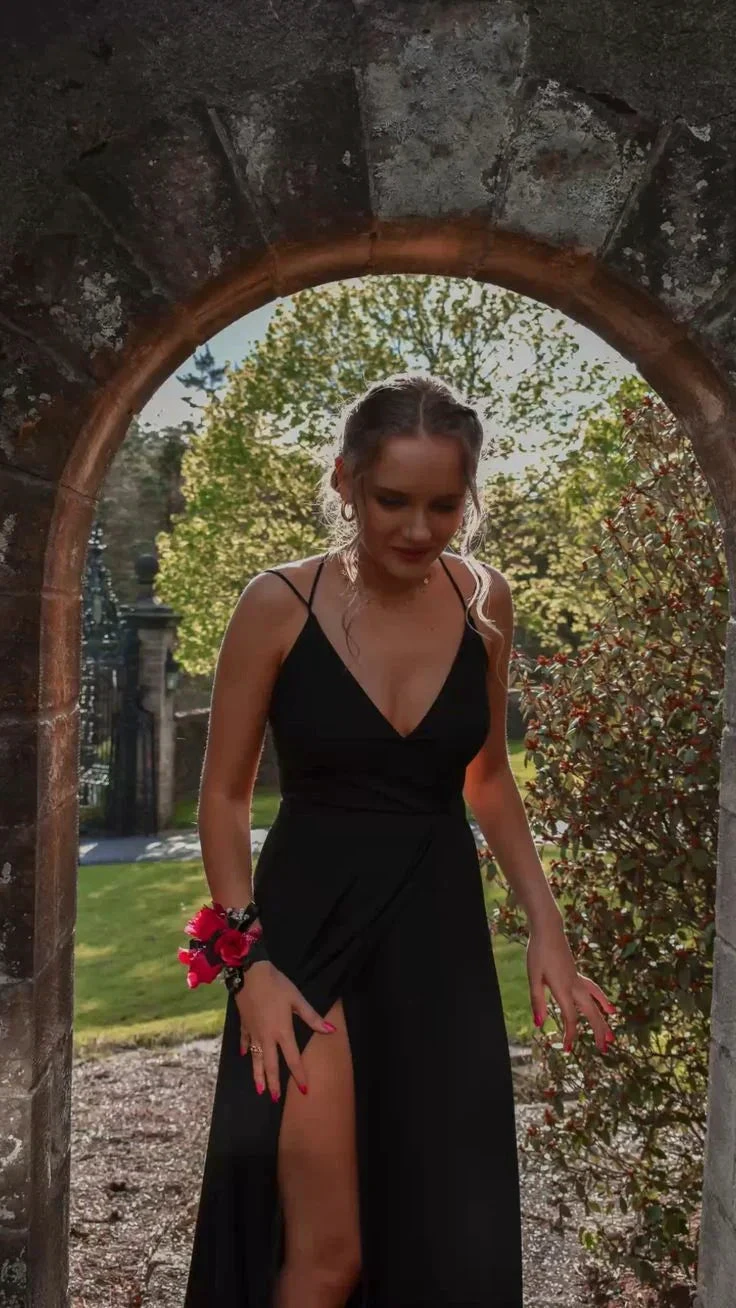 Woman in black evening dress with floral wrist corsage standing in stone archway outdoors, ZAPDRESS