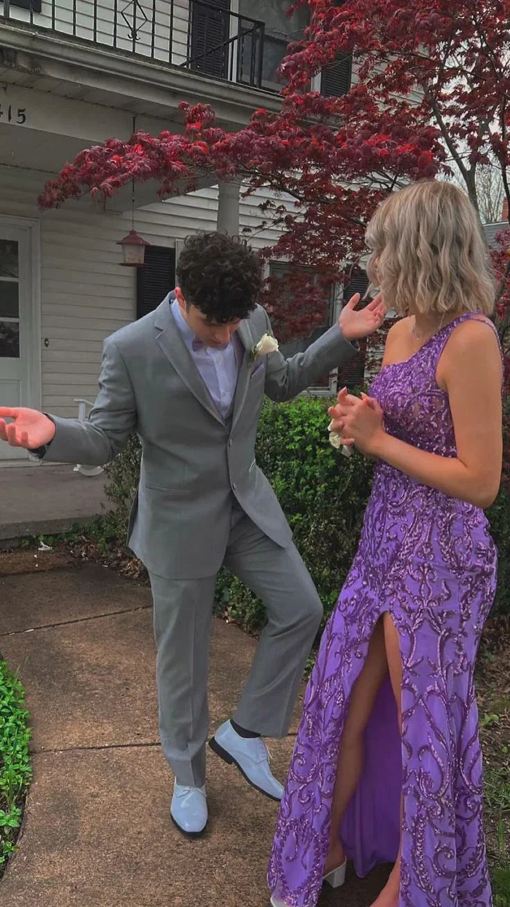 Young couple in formal attire, man in gray suit and woman in purple beaded dress, standing outside house near red-leafed tree