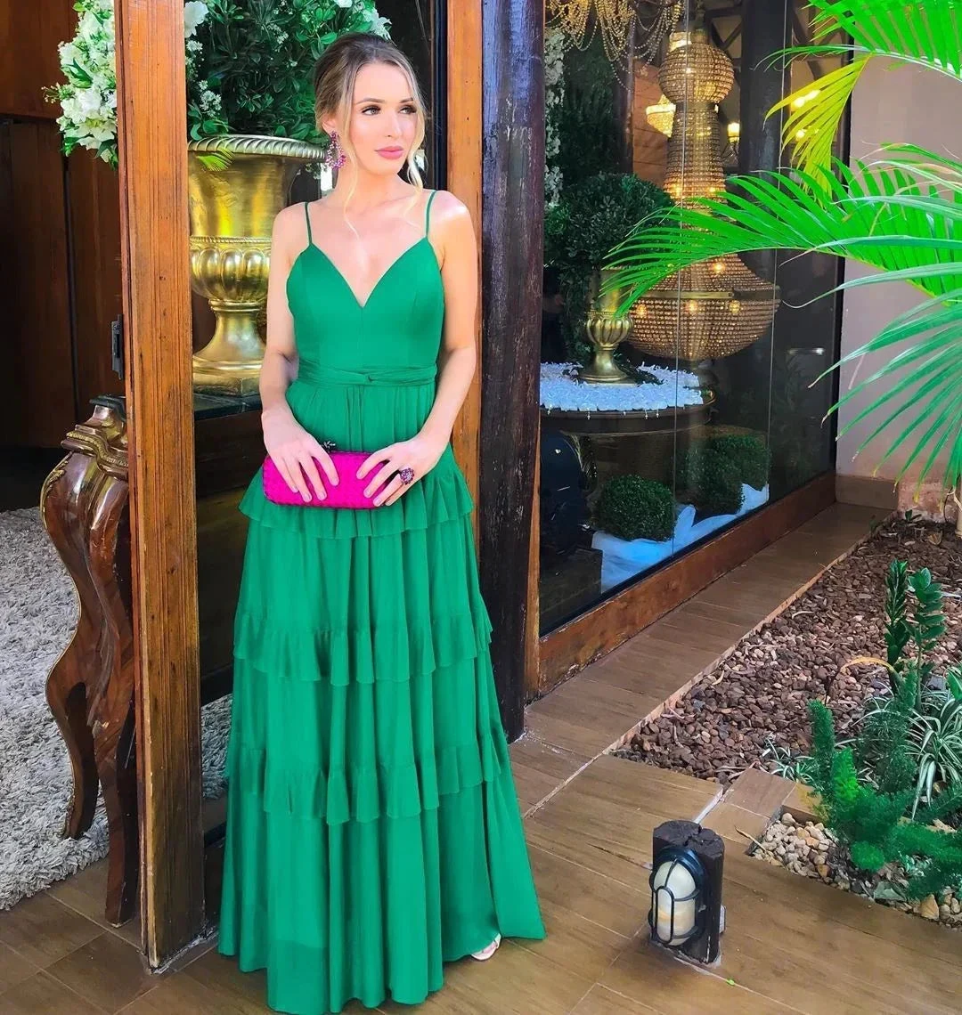 Woman in a green ruffle maxi dress holding a pink clutch, standing by a glass door at ZAPDRESS.