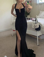 Woman wearing a black evening gown with a thigh-high slit in a bedroom, ZAPDRESS fashion.