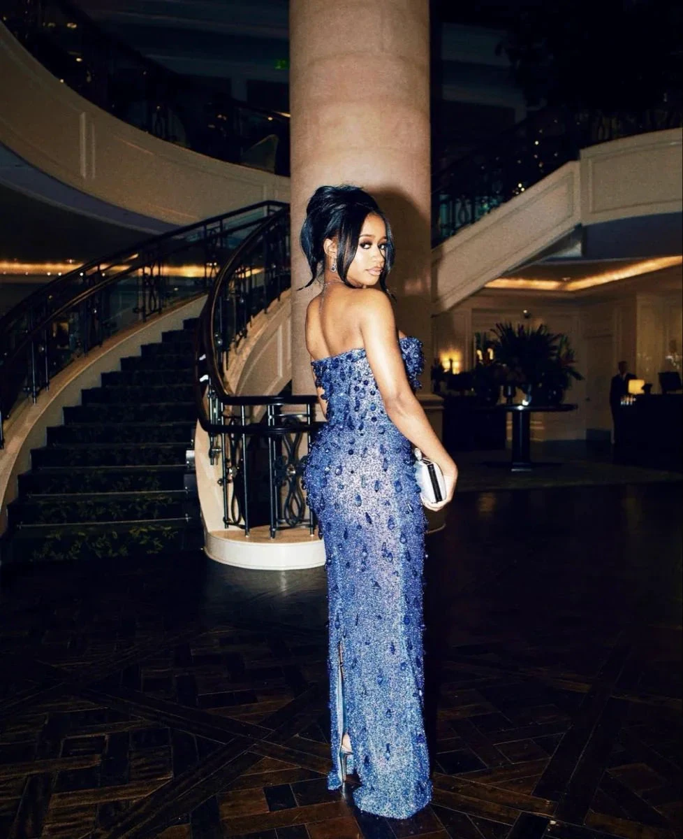 Woman in elegant blue sequin evening gown stands by luxury staircase at ZAPDRESS event.