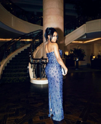 Woman in elegant blue sequin evening gown stands by luxury staircase at ZAPDRESS event.