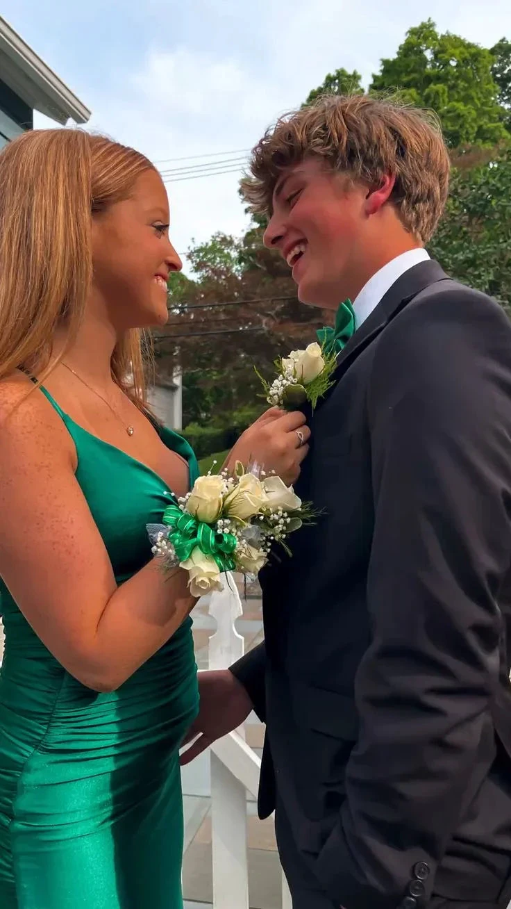 Couple in formal prom attire, woman in green dress, man in suit with green bow tie, smiling outdoors