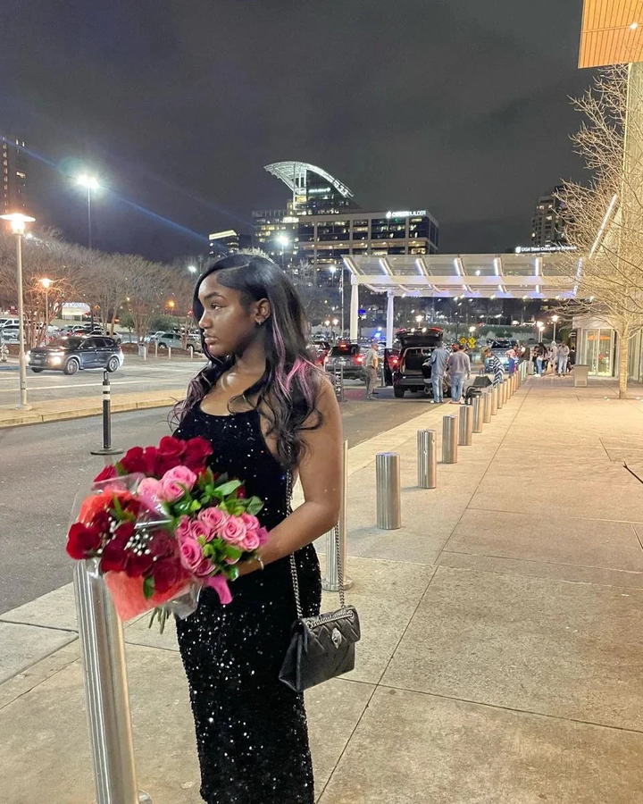 Woman in a black sequin dress holding red and pink roses outside at night, city lights in background, ZAPDRESS fashion