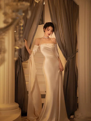 Elegant woman in a satin evening gown by ZAPDRESS standing between curtains on staircase