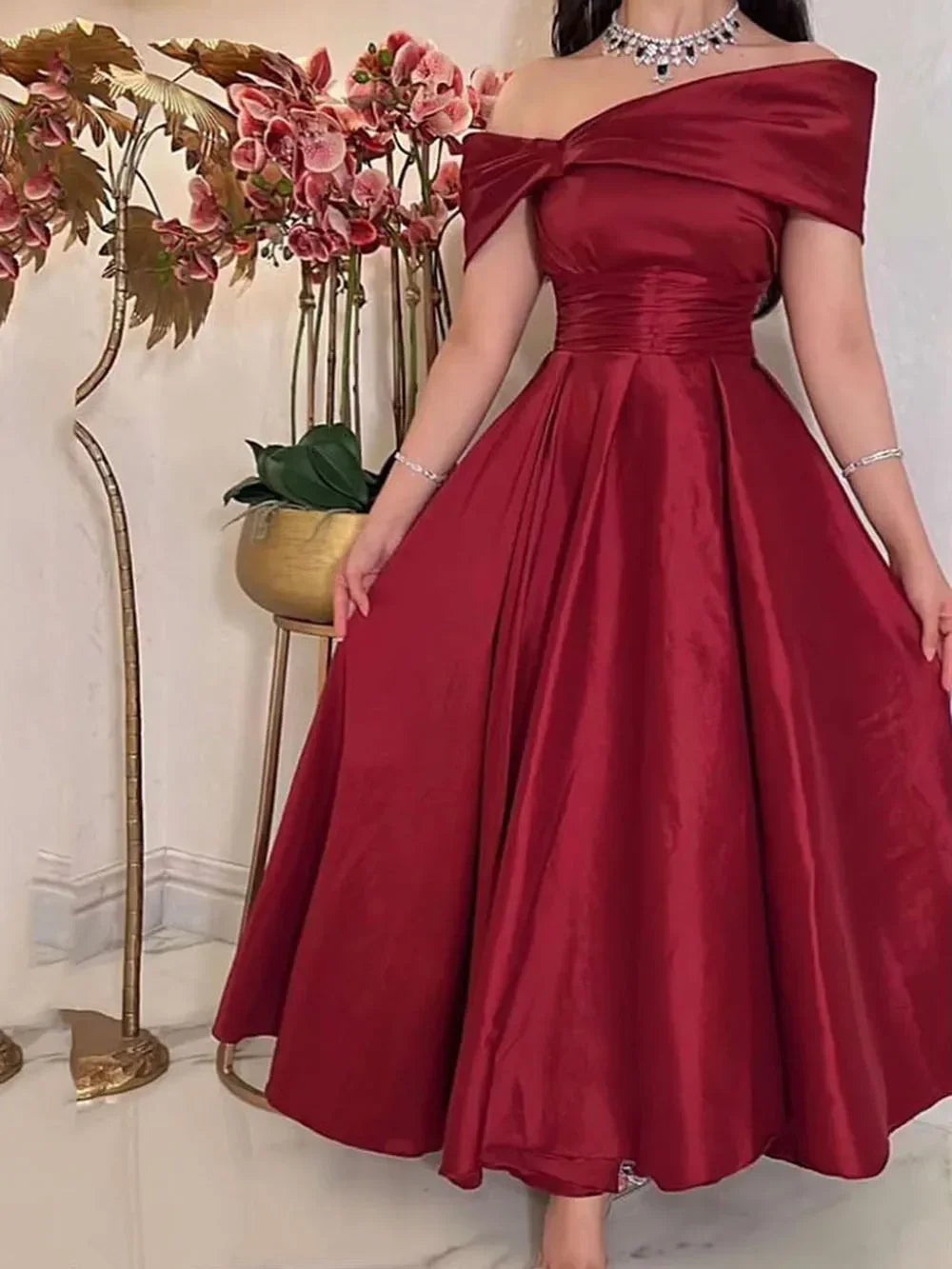 Elegant woman in off-shoulder red satin dress with floral backdrop at ZAPDRESS