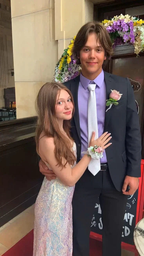 Young couple in formal attire with corsages, standing together at an event entrance with floral decor