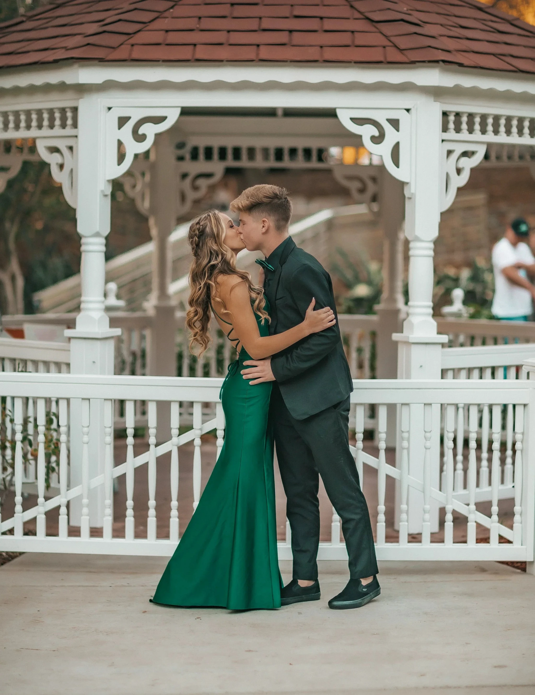 Couple in formal attire kissing at a white gazebo, woman in green dress, ZAPDRESS style