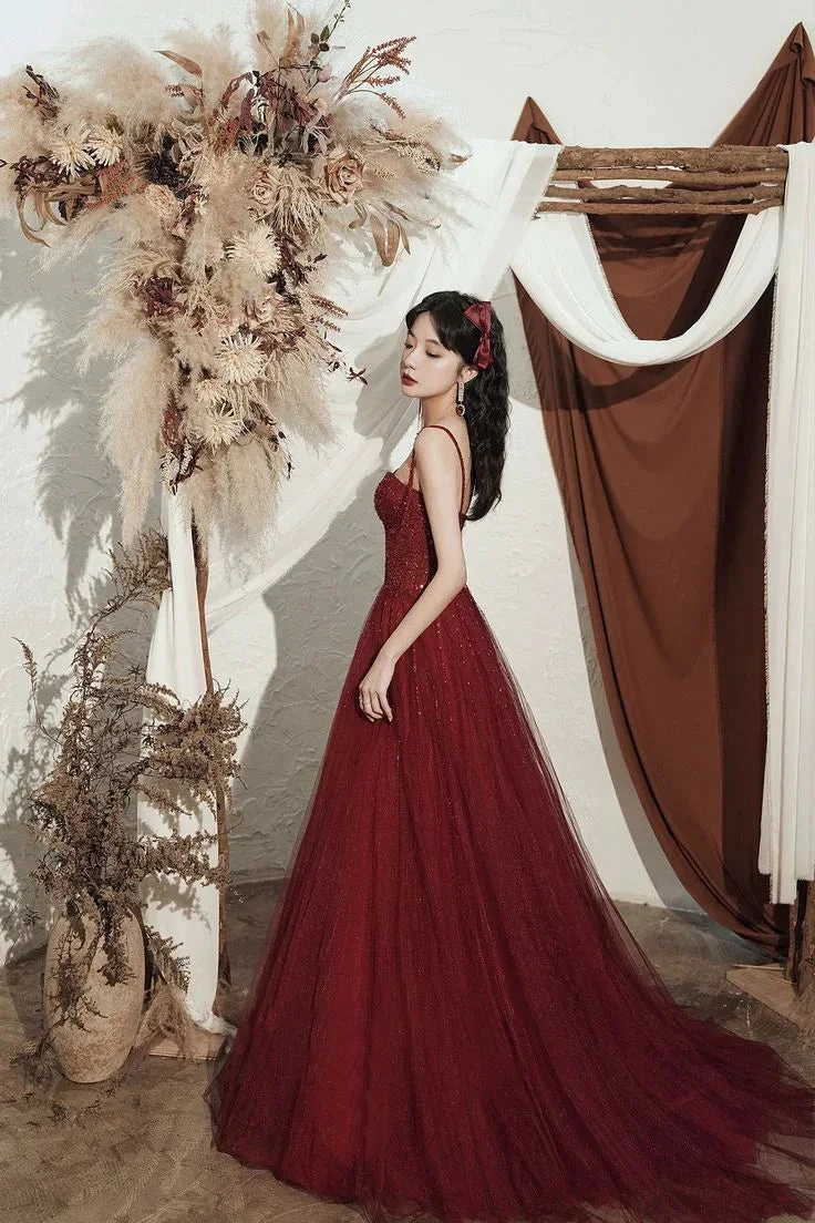 Elegant woman in a red evening gown by ZAPDRESS, posing indoors with dried floral decor