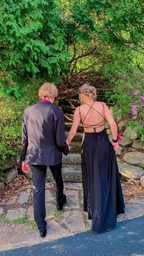 Couple in formal attire holding hands outdoors, woman in black backless dress from ZAPDRESS