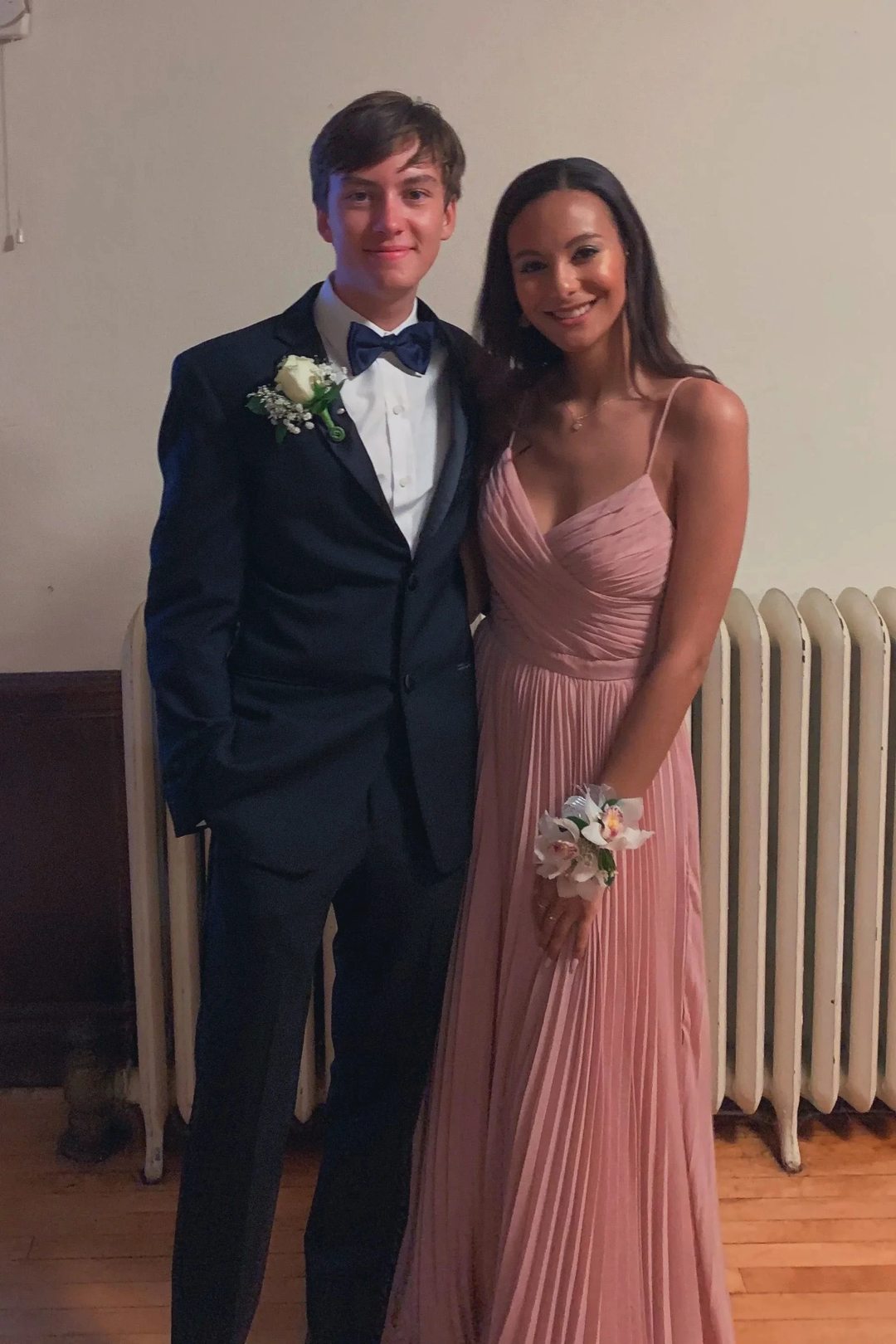 Young couple posing for prom, woman in pink pleated gown, man in black suit with boutonniere