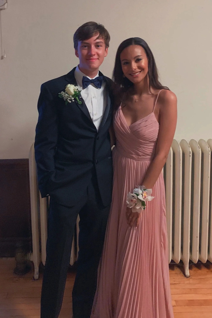 Young couple posing for prom, woman in pink pleated gown, man in black suit with boutonniere