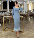 Woman in elegant light blue midi dress with feather hem poses in a luxurious banquet hall, ZAPDRESS