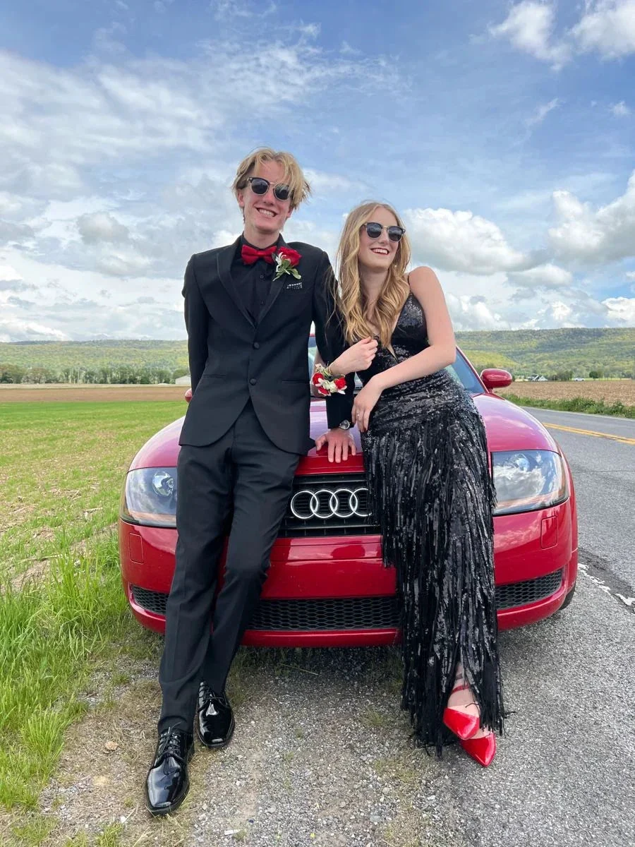 Smiling couple in formal attire leaning on red Audi, field and sky in background, ZAPDRESS style