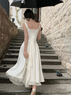 Woman in elegant white dress walking upstairs holding black umbrella, ZAPDRESS fashion.