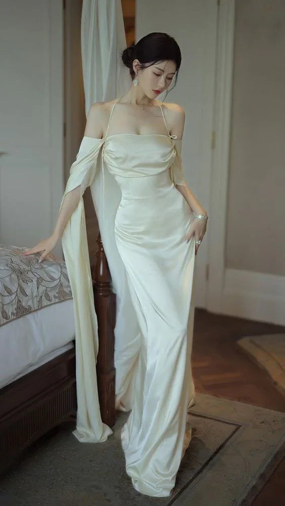 Elegant woman in a white satin evening gown by ZAPDRESS, standing in a bedroom setting
