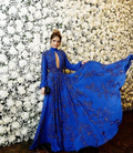 Woman in an elegant royal blue embellished gown posing by a white flower wall, ZAPDRESS style