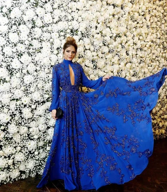 Woman in an elegant royal blue embellished gown posing by a white flower wall, ZAPDRESS style