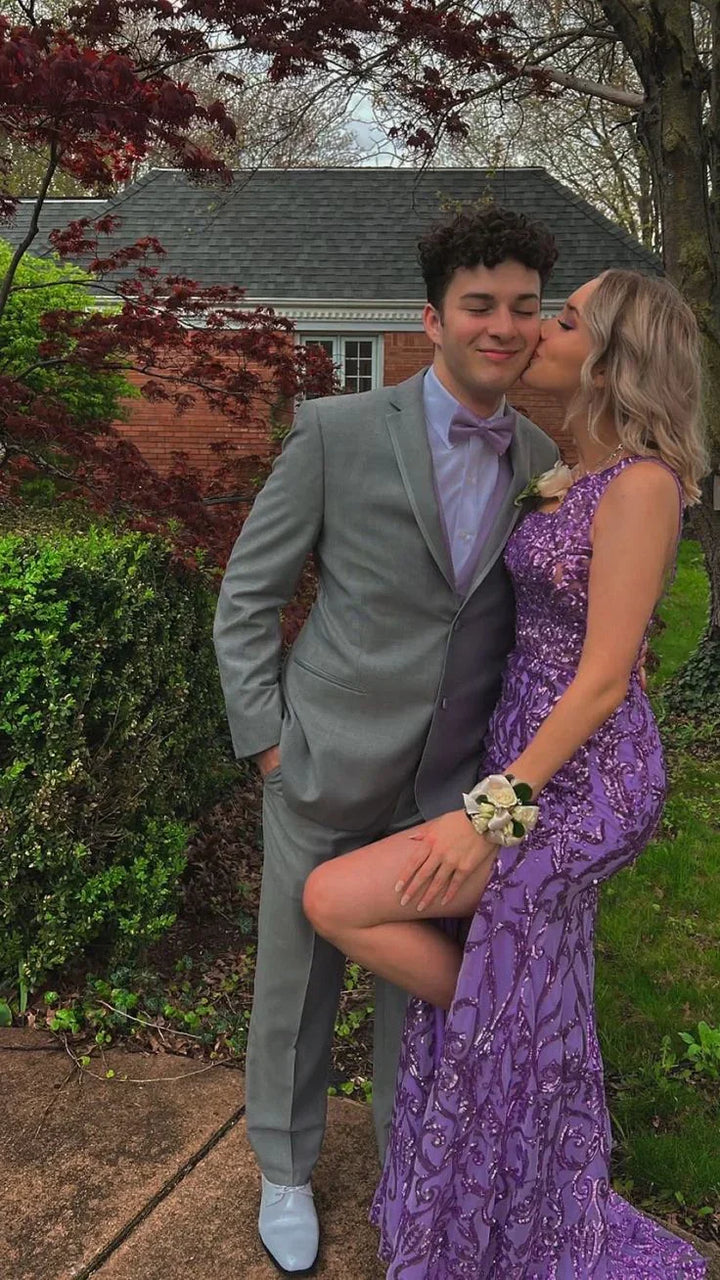Couple in formal attire, woman in purple sequin prom dress kissing man in gray suit, outdoor garden
