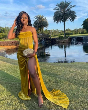 Woman in yellow strapless evening gown posing outdoors by a pond, palm trees, and bridge