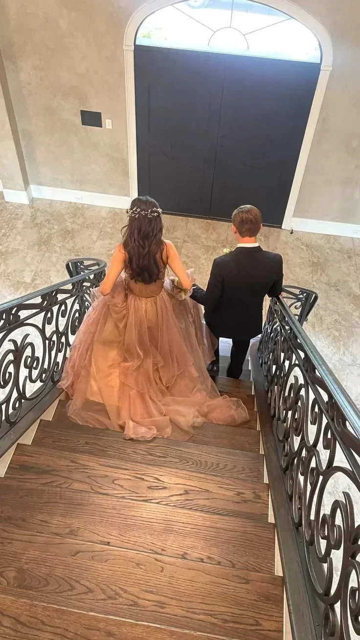 Woman in elegant brown ball gown and man in suit walking down staircase, ZAPDRESS formalwear