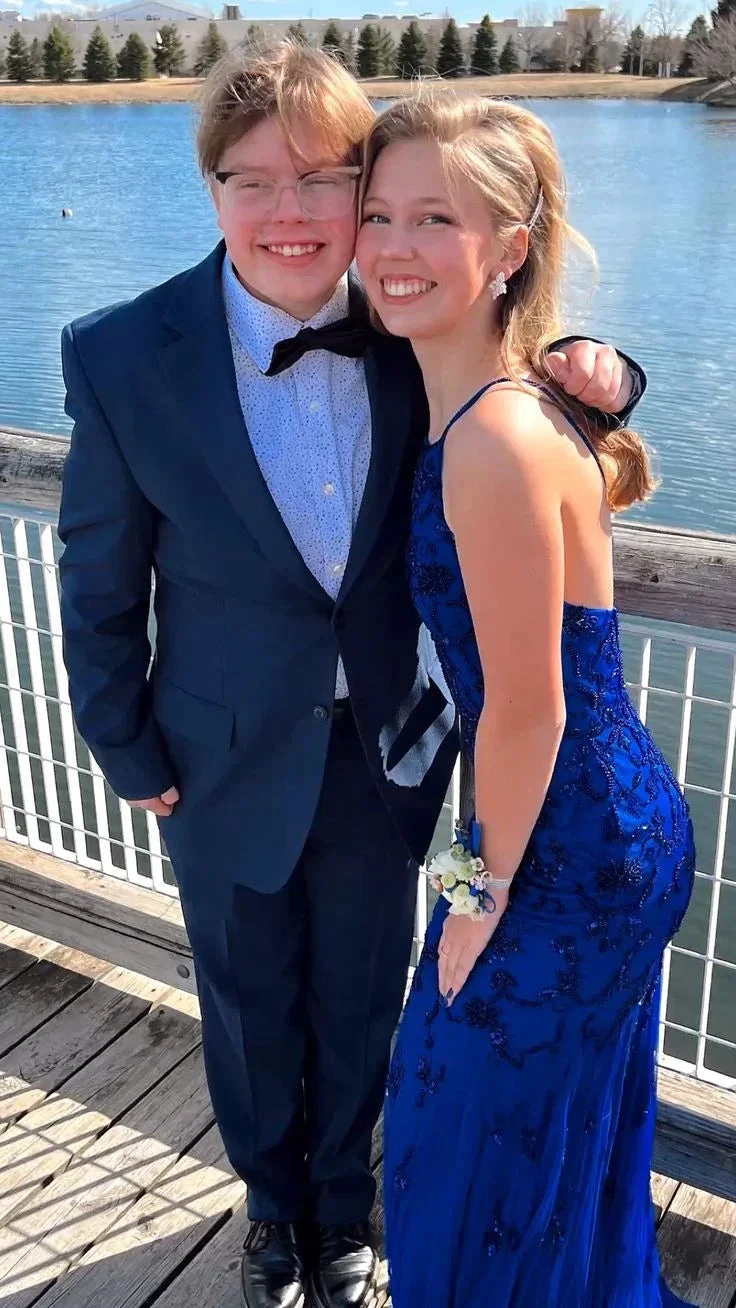 Young couple in formal attire posing by a lake, woman in blue evening dress, ZAPDRESS style.