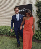 Couple dressed formally, man in navy suit, woman in one-shoulder orange dress, outdoors