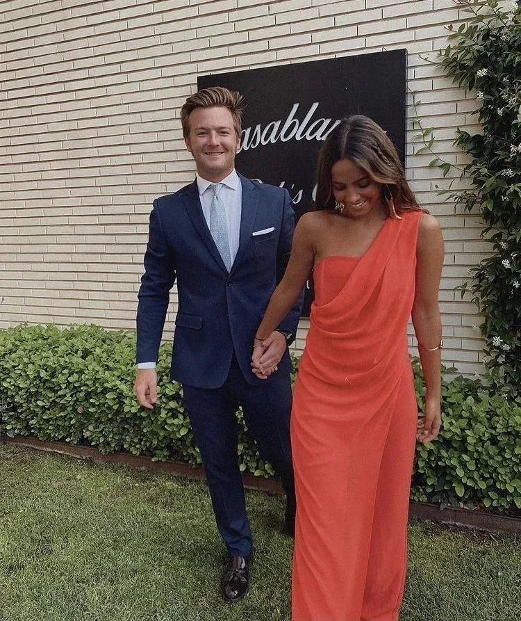 Couple dressed formally, man in navy suit, woman in one-shoulder orange dress, outdoors