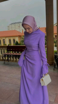 Woman wearing elegant lilac modest dress and matching hijab, holding white handbag outdoors