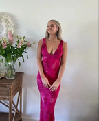 Woman in a deep pink sleeveless dress stands beside flowers, white wall background, ZAPDRESS