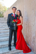 Couple in formal attire, woman in long red dress, holding bouquet, standing on marble stairs