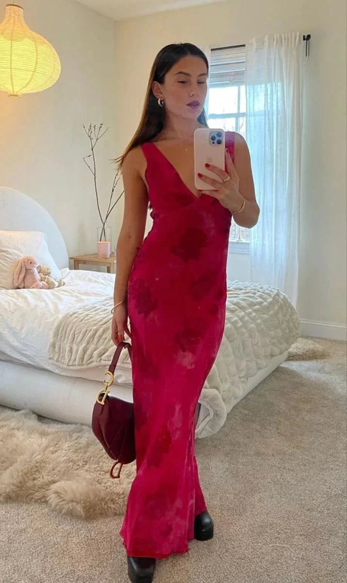 Woman in a red sleeveless maxi dress holding a handbag, taking a mirror selfie in a bedroom