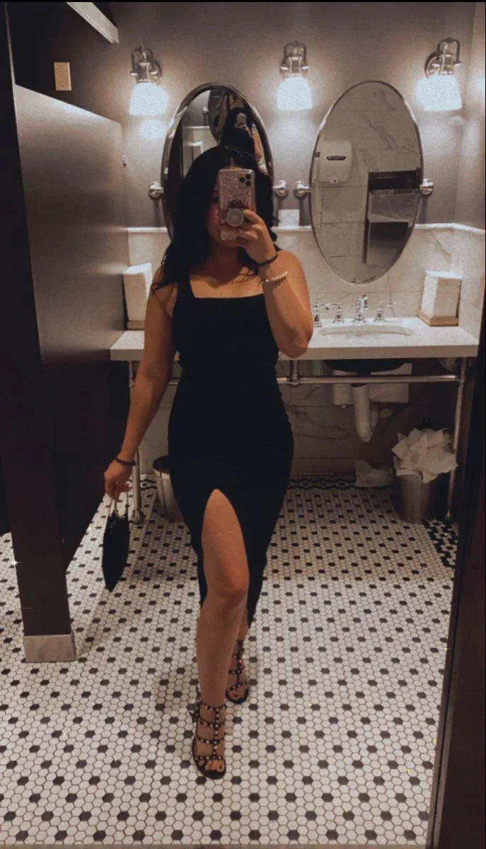 Woman in black dress with thigh-high slit taking mirror selfie in stylish restroom