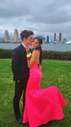 Couple posing outdoors, woman in bright pink prom dress, city skyline in background, ZAPDRESS fashion