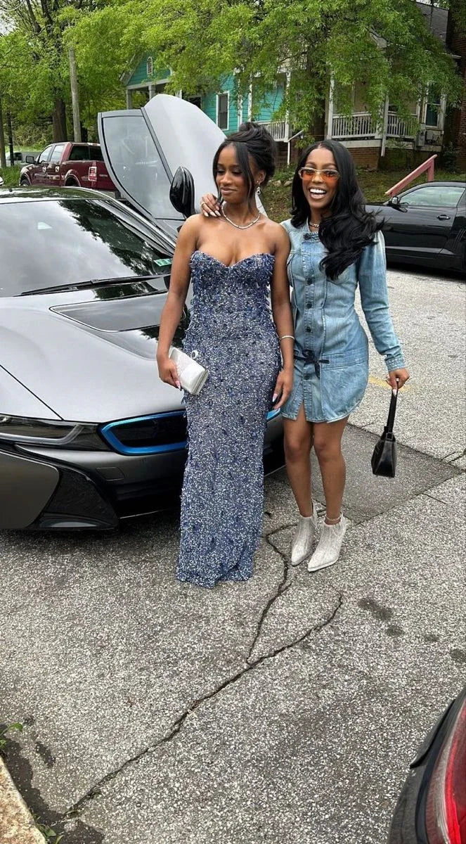 Two stylish women posing by a luxury car, one in a sparkly gown, one in denim dress