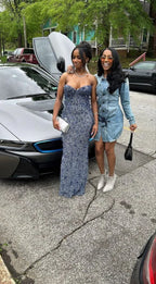 Two stylish women posing by a luxury car, one in a sparkly gown, one in denim dress