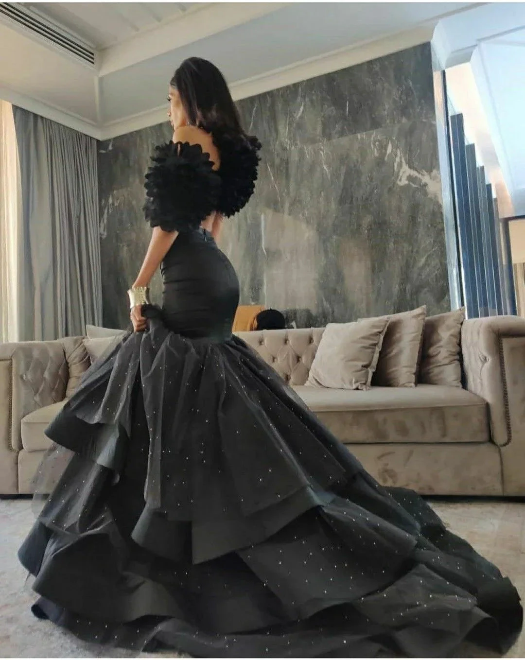 Elegant woman in a black ruffled ball gown in modern living room, ZAPDRESS fashion.