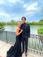 Young couple in formal black attire posing by a lake with elegant railing, ZAPDRESS style