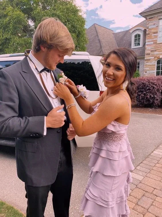 Smiling couple in formal attire outside, woman in lilac dress helps man with boutonniere, ZAPDRESS style