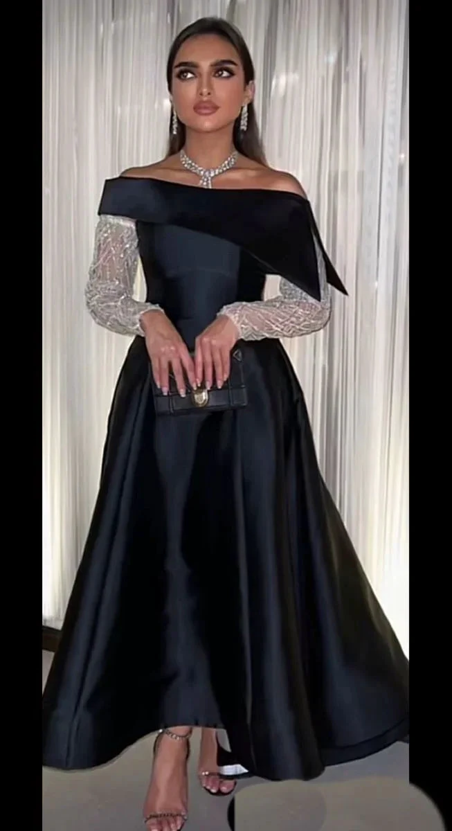 Elegant woman in off-shoulder black Zapdress gown with sheer long sleeves, evening setting