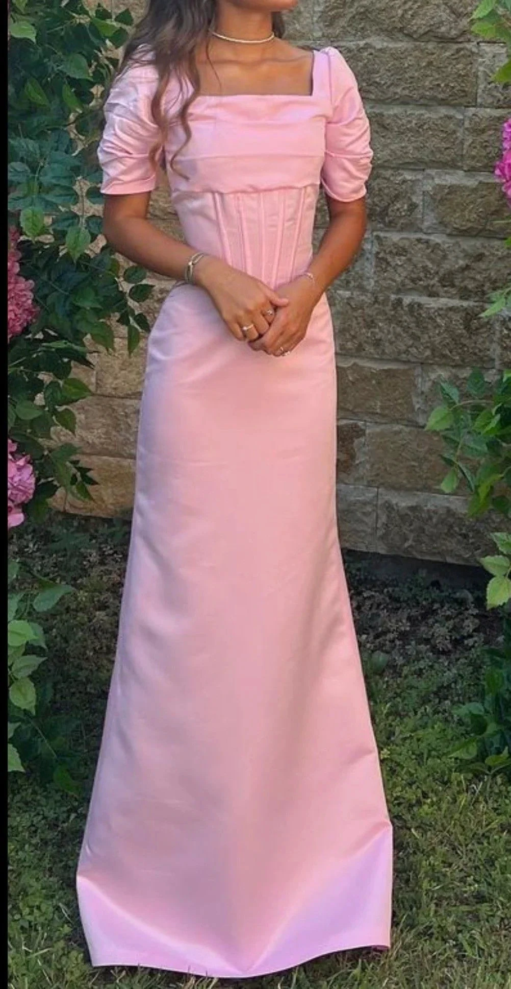 Woman wearing a long pink puff sleeve dress from ZAPDRESS, standing outdoors by a stone wall