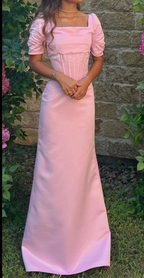 Woman wearing a long pink puff sleeve dress from ZAPDRESS, standing outdoors by a stone wall