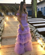 Woman in a lilac ruffle off-shoulder dress standing on a floral-lit walkway, evening event