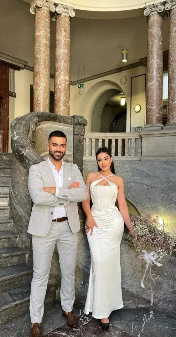Man in light grey suit and woman in elegant white dress posing by marble staircase at ZAPDRESS