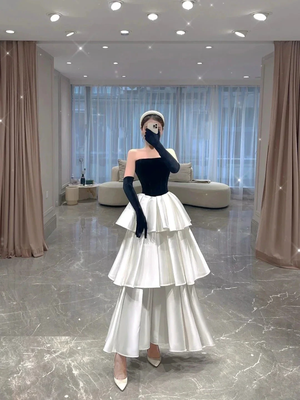 Elegant woman in a tiered black and white evening dress with gloves in a modern living room, ZAPDRESS fashion