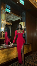 Woman in elegant red evening gown with high slit, standing by mirror in a modern, upscale interior